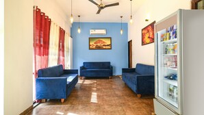 A hotel lobby with a blue sofa set, a ceiling fan, and a beverage refrigerator. - Fabhotel Shrivalli (Indore)