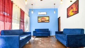 A room with two blue sofas, a wooden floor, a blue wall, an air conditioning unit, and a framed painting. - Fabhotel Shrivalli (Indore)