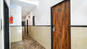 A hallway with a marble floor, a wooden door with a number plate, and a fire extinguisher mounted on the wall. - Fabhotel Shrivalli (Indore)
