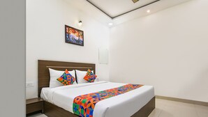 A modern hotel room with a large bed, a nightstand, a wall-mounted painting, and a mirror. - Fabhotel Shrivalli (Indore)