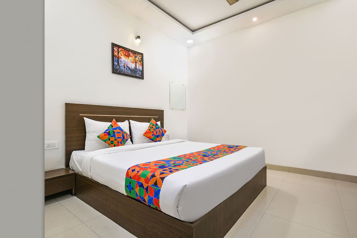 A modern hotel room with a large bed, a nightstand, a wall-mounted painting, and a mirror.