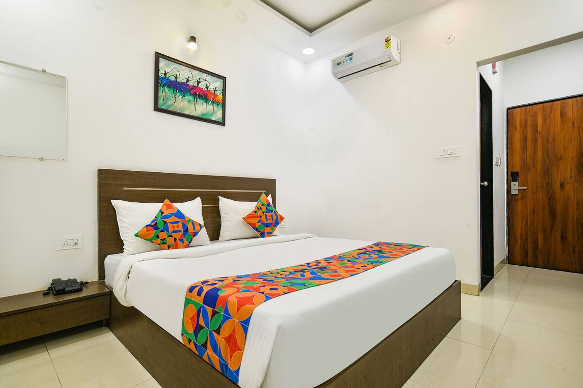 A neatly made bed with a colorful bedspread, a wooden headboard, and a single wall-mounted air conditioner.