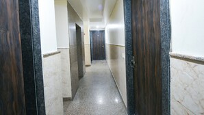 A hallway with marble flooring, wooden doors, and a plain wall. - Fabhotel Moon Light (New Delhi)