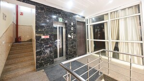 A hotel lobby with marble walls, a staircase, and a glass elevator. - Fabhotel Moon Light (New Delhi)
