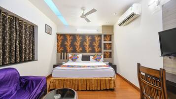 A hotel room with a bed, a chair, a table, a ceiling fan, an air conditioner, and a TV.