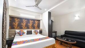 A hotel room with a bed, a black leather sofa, a ceiling fan, and a wall with a leaf pattern. - Fabhotel Raj Matrya Inn (Patna)