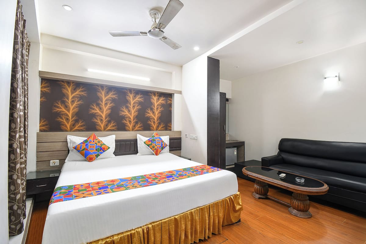 A hotel room with a bed, a black leather sofa, a ceiling fan, and a wall with a leaf pattern.