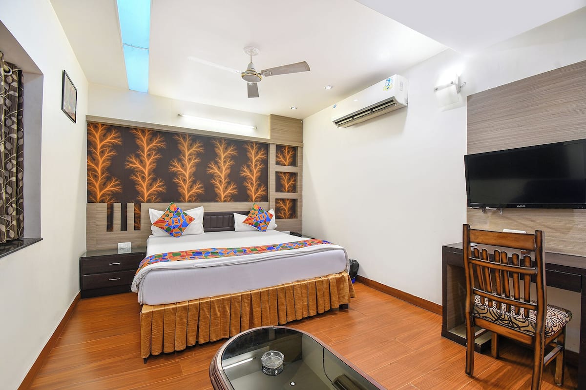 A hotel room with a bed, a desk, a chair, a ceiling fan, and a TV.