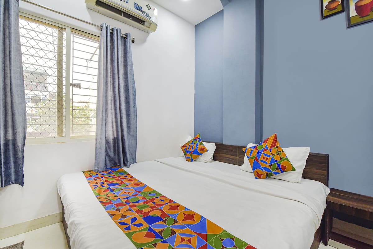 A hotel room with a bed, two pillows, a window with curtains, and an air conditioning unit.