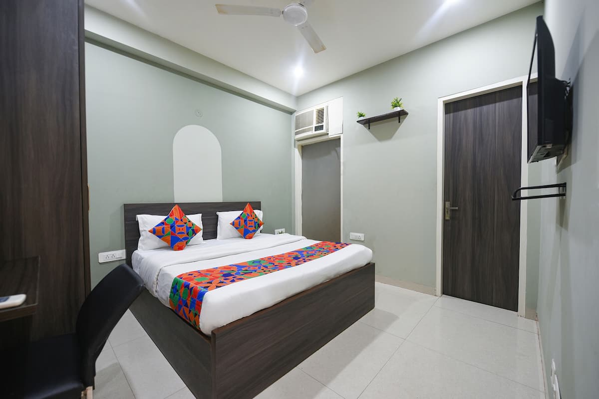 A modern bedroom with a large bed, a ceiling fan, a TV mounted on the wall, and a small shelf with a plant.