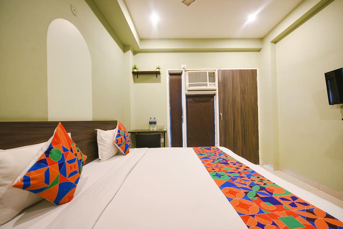 A hotel room with a bed, pillows, a nightstand, a TV, and a wardrobe.