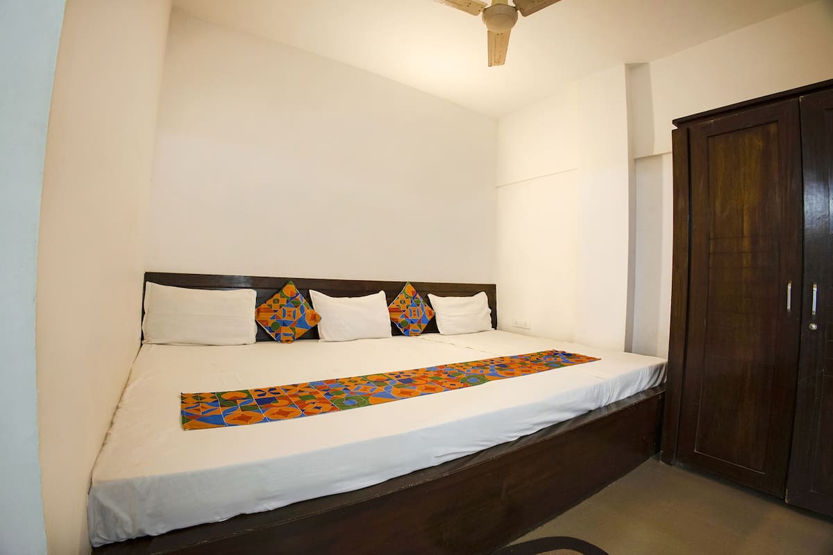 A single bed with a wooden headboard, white bedding, and a colorful geometric throw blanket.