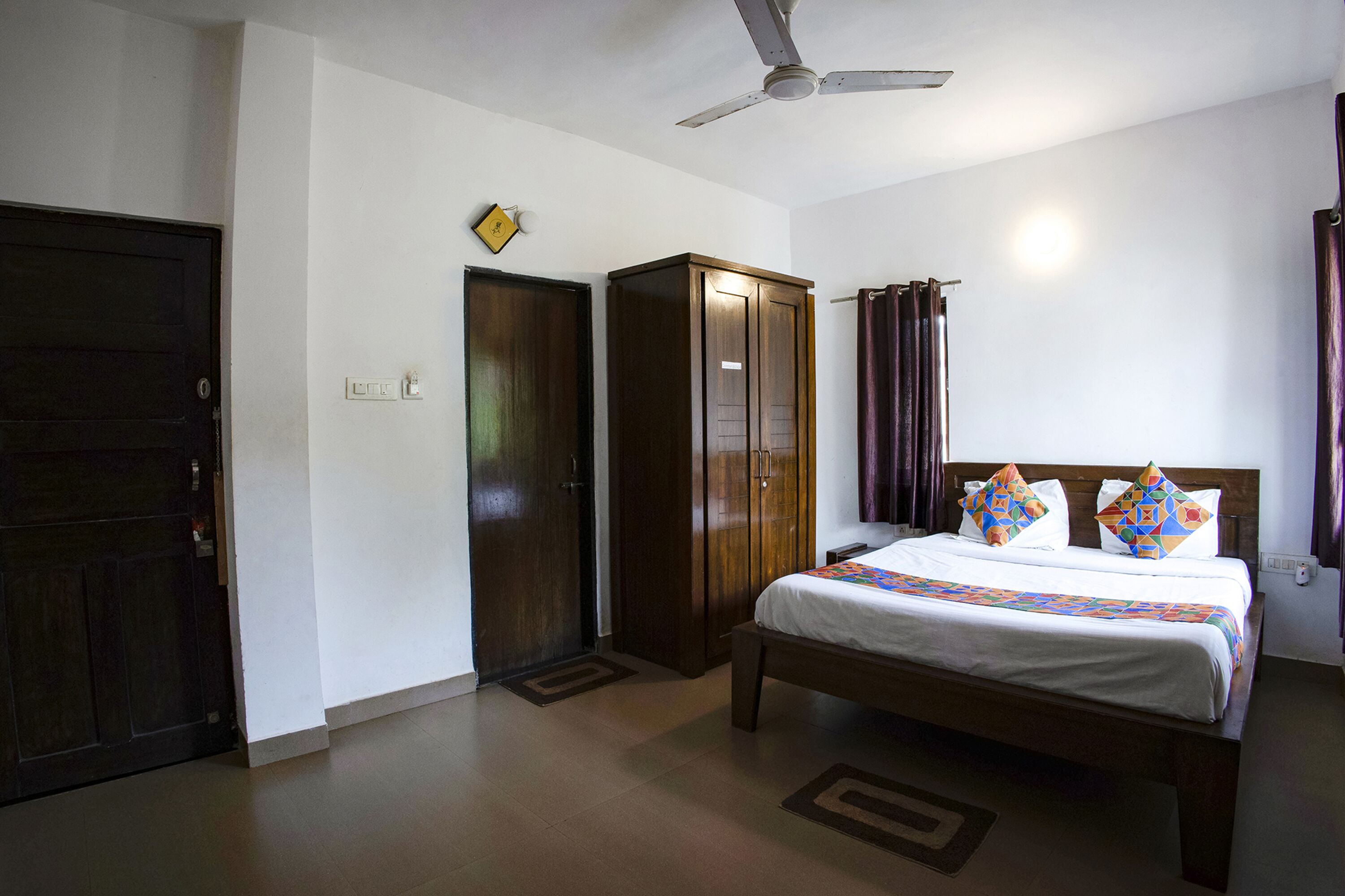 A hotel room with a bed, wardrobe, ceiling fan, and curtains.
