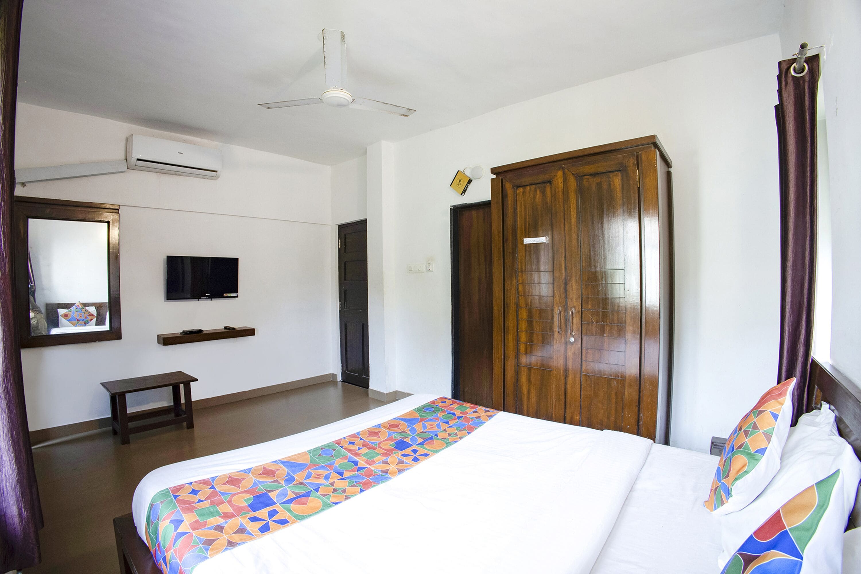 A hotel room with a bed, a wooden wardrobe, a television, and a ceiling fan.