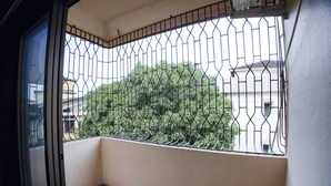 A balcony with a metal railing, a view of a tree, and a building in the background. - Fabhotel Comfort Stays (Panaji)