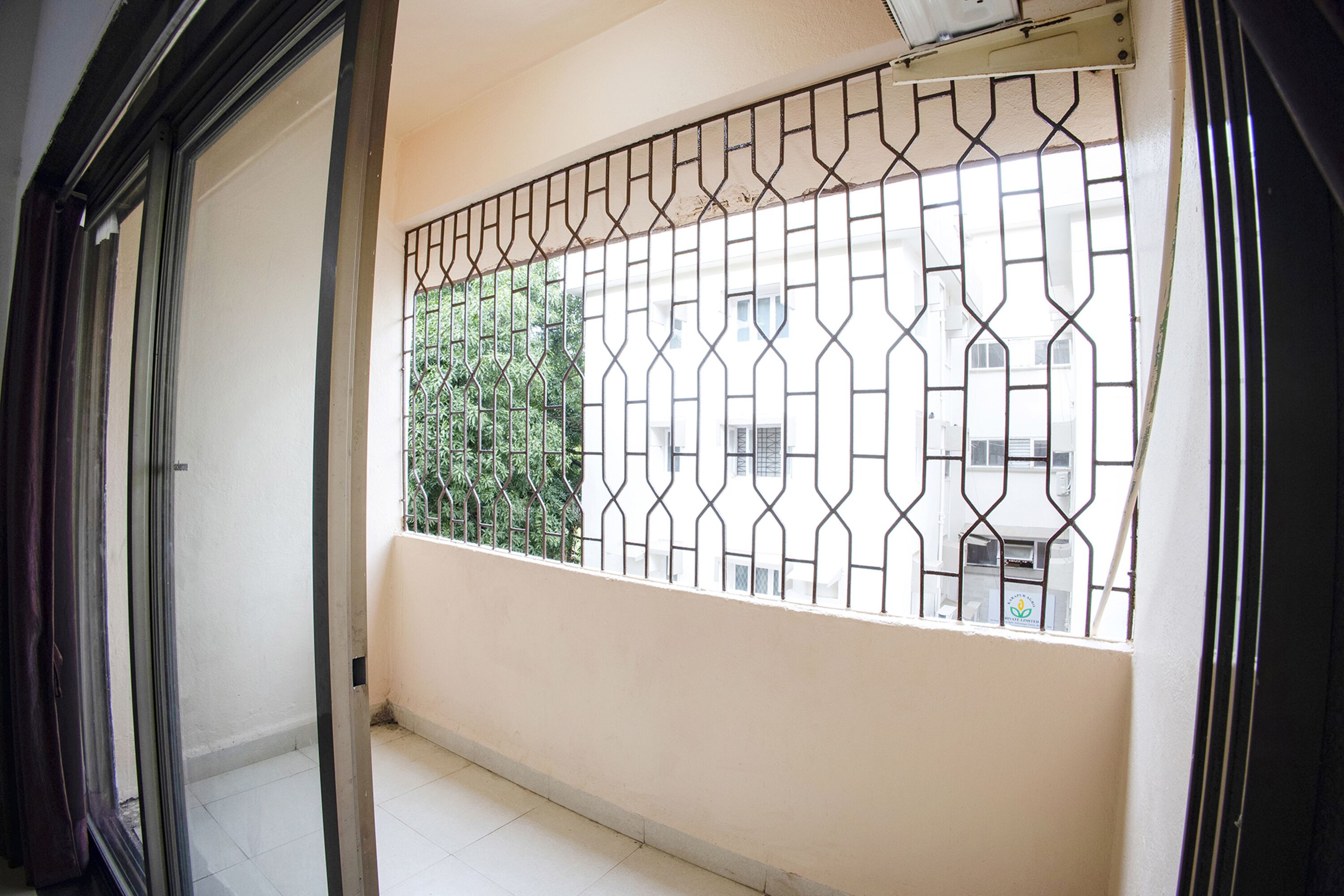 A balcony with a metal security gate, a white wall, and a view of a building with air conditioning units.