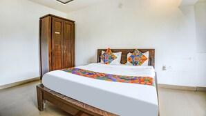 A bedroom with a bed, wooden wardrobe, and a white wall. - Fabhotel Comfort Stays (Panaji)