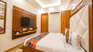 A bedroom with a bed, a mounted TV, a wooden shelf with flowers, and a ceiling light. - Fabhotel Shree Jii Luxury (New Delhi)