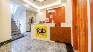 A hotel reception area with a marble staircase, a reception desk with a 'Tab Hotels' sign, an air conditioning unit, and a wooden door. - Fabhotel Shree Jii Luxury (New Delhi)