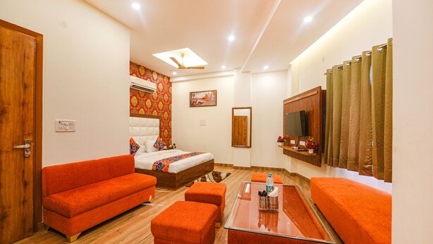 A hotel room with a bed, orange sofa, ottomans, a glass coffee table, a TV, and a shower curtain. - Fabhotel Shree Jii Luxury (New Delhi)