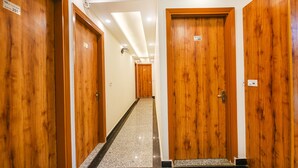 A hotel hallway with wooden doors, a tiled floor, and a ceiling with recessed lighting. - Fabhotel Shree Jii Luxury (New Delhi)