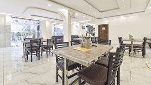 A spacious dining area with multiple tables and chairs, a central pillar with a fan, and a view of the outside through large windows. - Fabhotel Dev Palace (Haridwar)