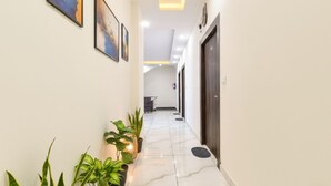 A hallway with a marble floor, potted plants, framed artwork, and a door at the end. - Fabhotel Dev Palace (Haridwar)