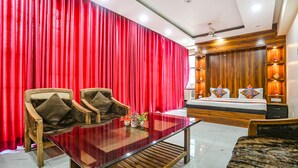 Una habitación con un telón rojo de fondo, una cama de madera con almohadas, una mesa de centro de vidrio y dos sillas de madera.