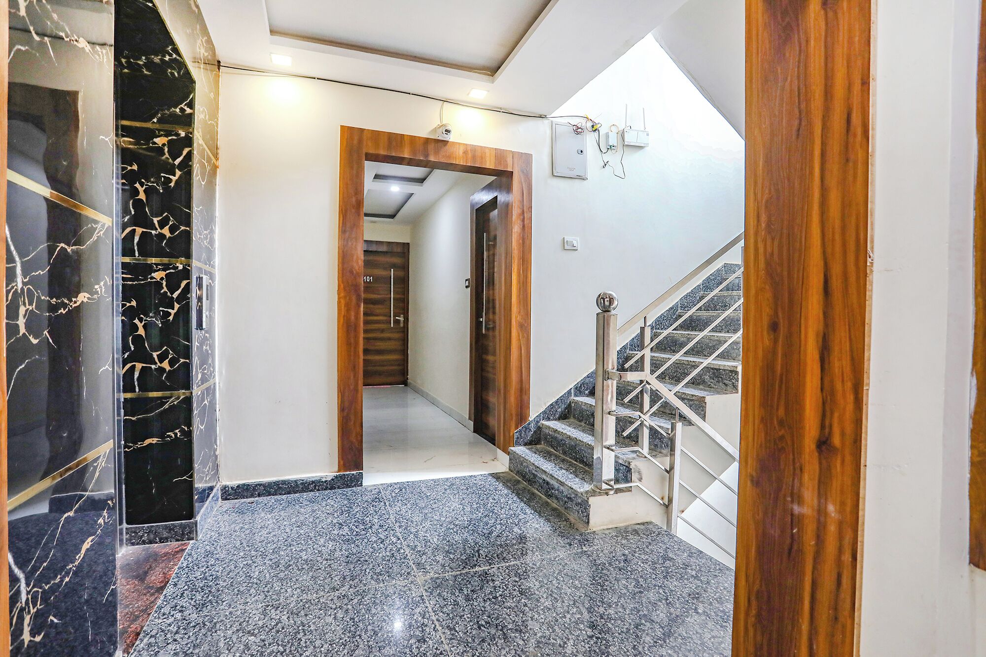 A hallway with a marble floor, a wooden door, and a staircase with metal railings.