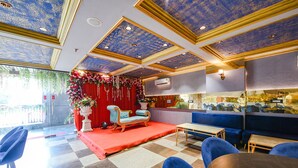 A hotel lobby with a checkered floor, blue seating, a stage with red curtains, and a decorative floral arrangement. - Fabhotel Prime Apple Tree Residency (New Delhi)