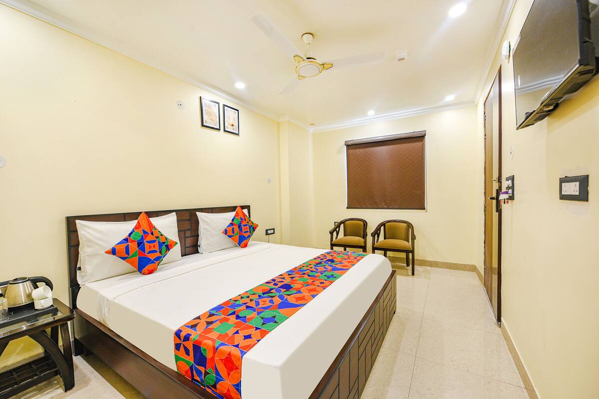 A hotel room with a bed, a desk, chairs, a ceiling fan, and a window.