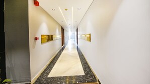 A long, narrow hallway with a marble floor and white walls. There are doors on both sides and a sign on the right wall. - Fabhotel Prime Apple Tree Residency (New Delhi)