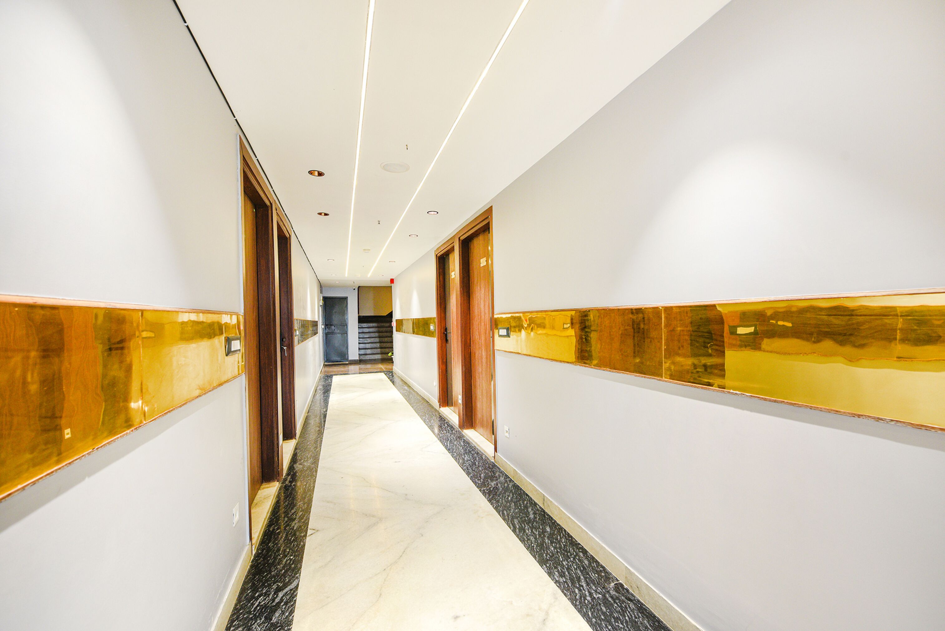 A hallway with marble flooring, wooden doors, and gold-framed mirrors on the walls.