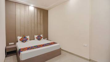 A bedroom with a bed, a nightstand, a wall-mounted panel, and a power outlet.