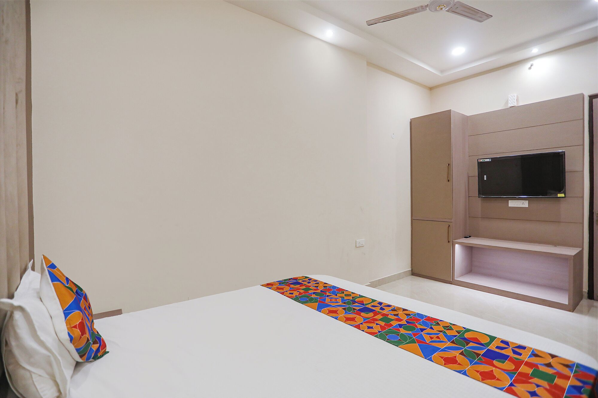 A bedroom with a bed, a TV mounted on a wall, and a ceiling fan.
