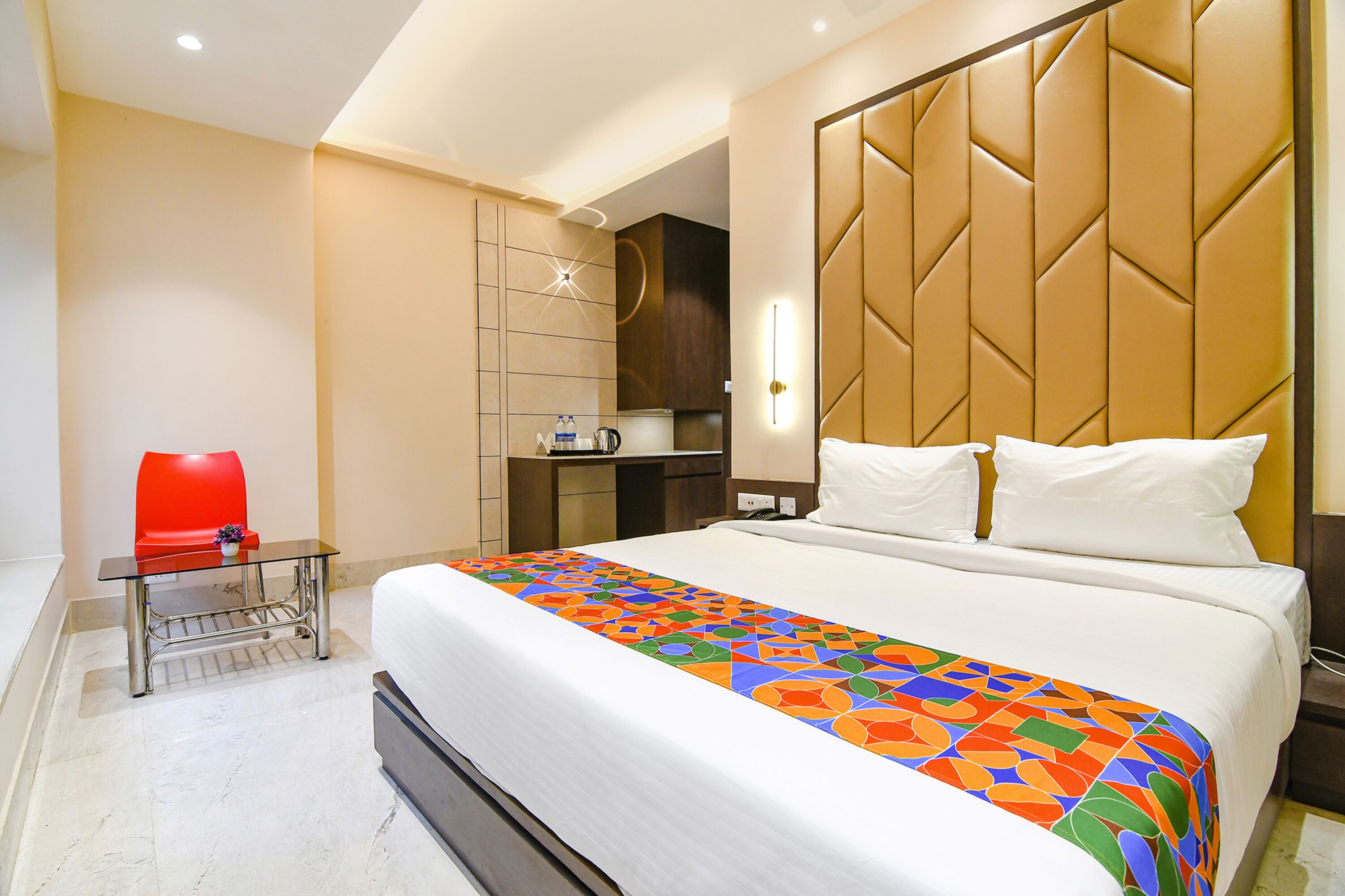 A hotel room with a bed, a red chair, a small table, and a nightstand.