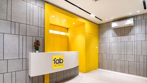 Un espace d’accueil au design moderne, comprenant un comptoir de réception portant l’inscription « fab hotels » et un mur d’accent d’un jaune vif.