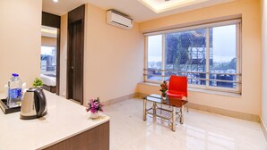 Une chambre d’hôtel avec une grande fenêtre, un ventilateur de plafond, une machine à café et une petite table avec une chaise rouge.