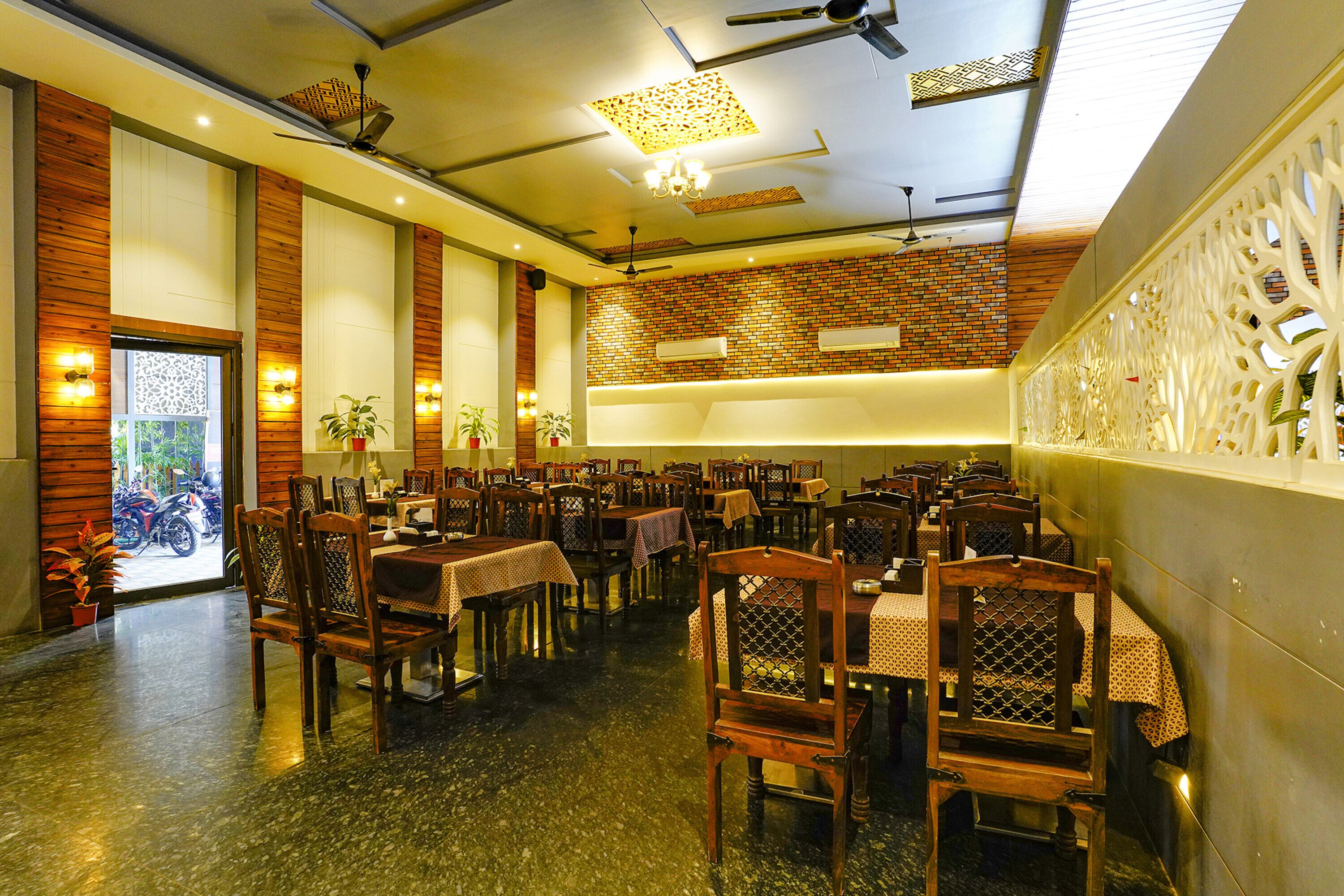 A restaurant with multiple tables and chairs, a brick wall, and ceiling fans.