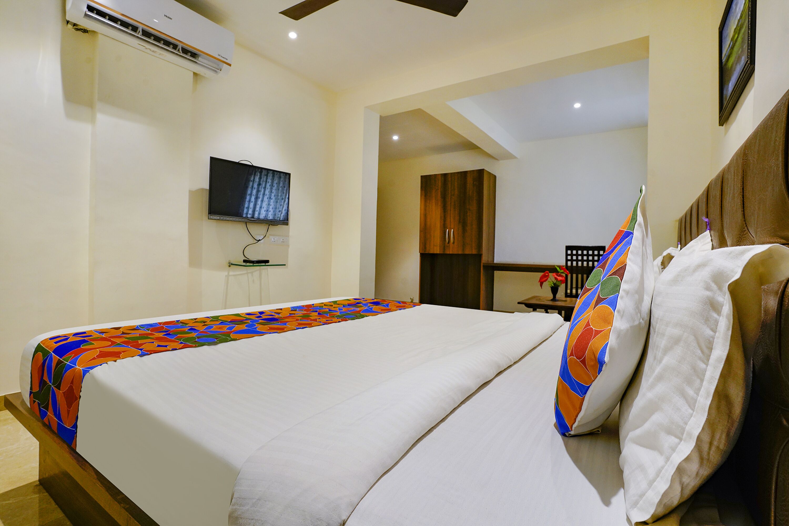 Una habitación de hotel con cama, televisor, armario de madera y una pequeña mesa con un florero.