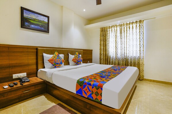 A hotel room with a wooden headboard, a bed with a colorful geometric bedspread, a nightstand with a phone and remote, and a painting on the wall. - Fabhotel Prime Hangout (Pune)
