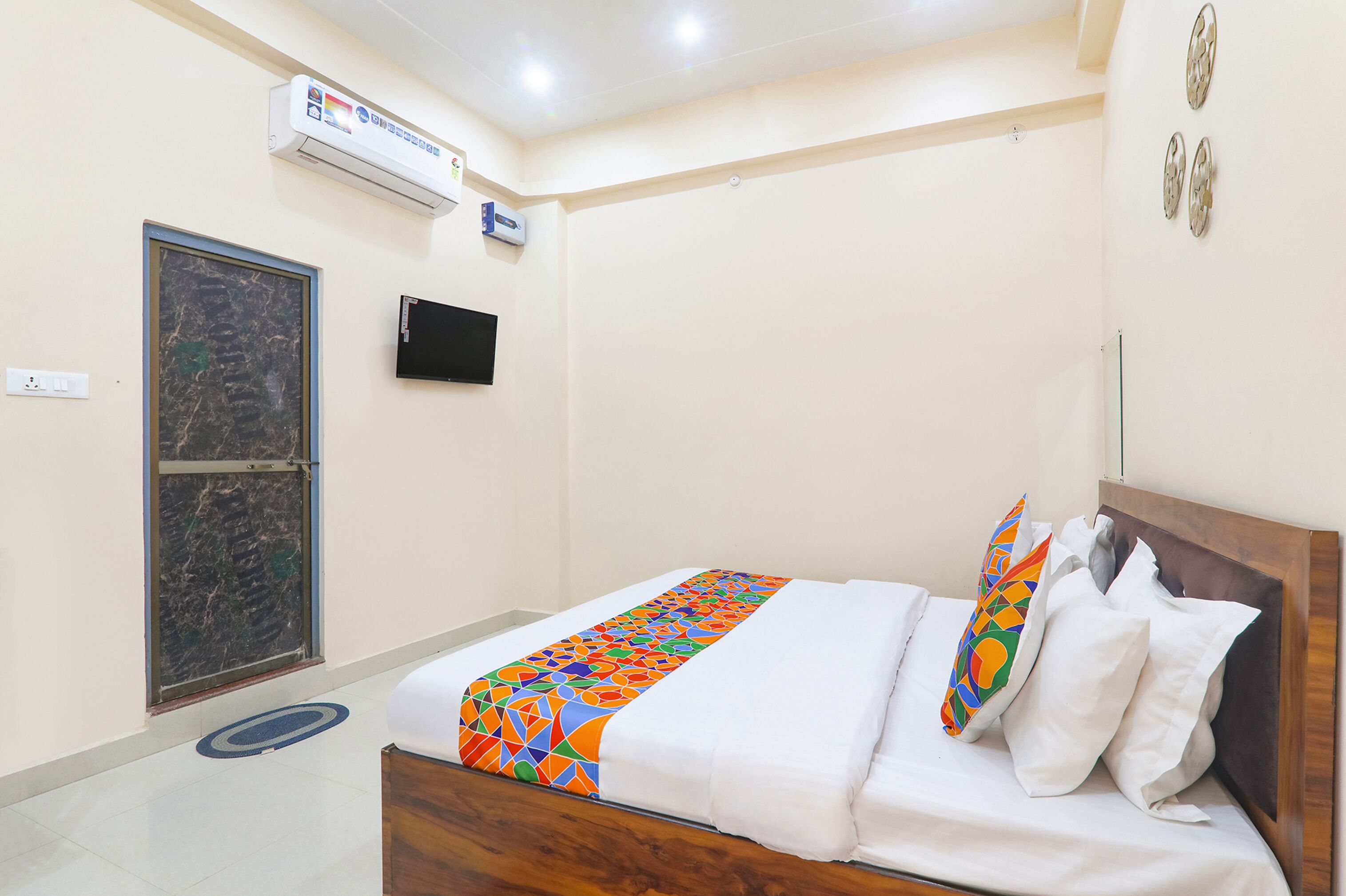 Hotelkamer met een bed, een televisie, een airconditioningapparaat, een deur en een wandlamp.