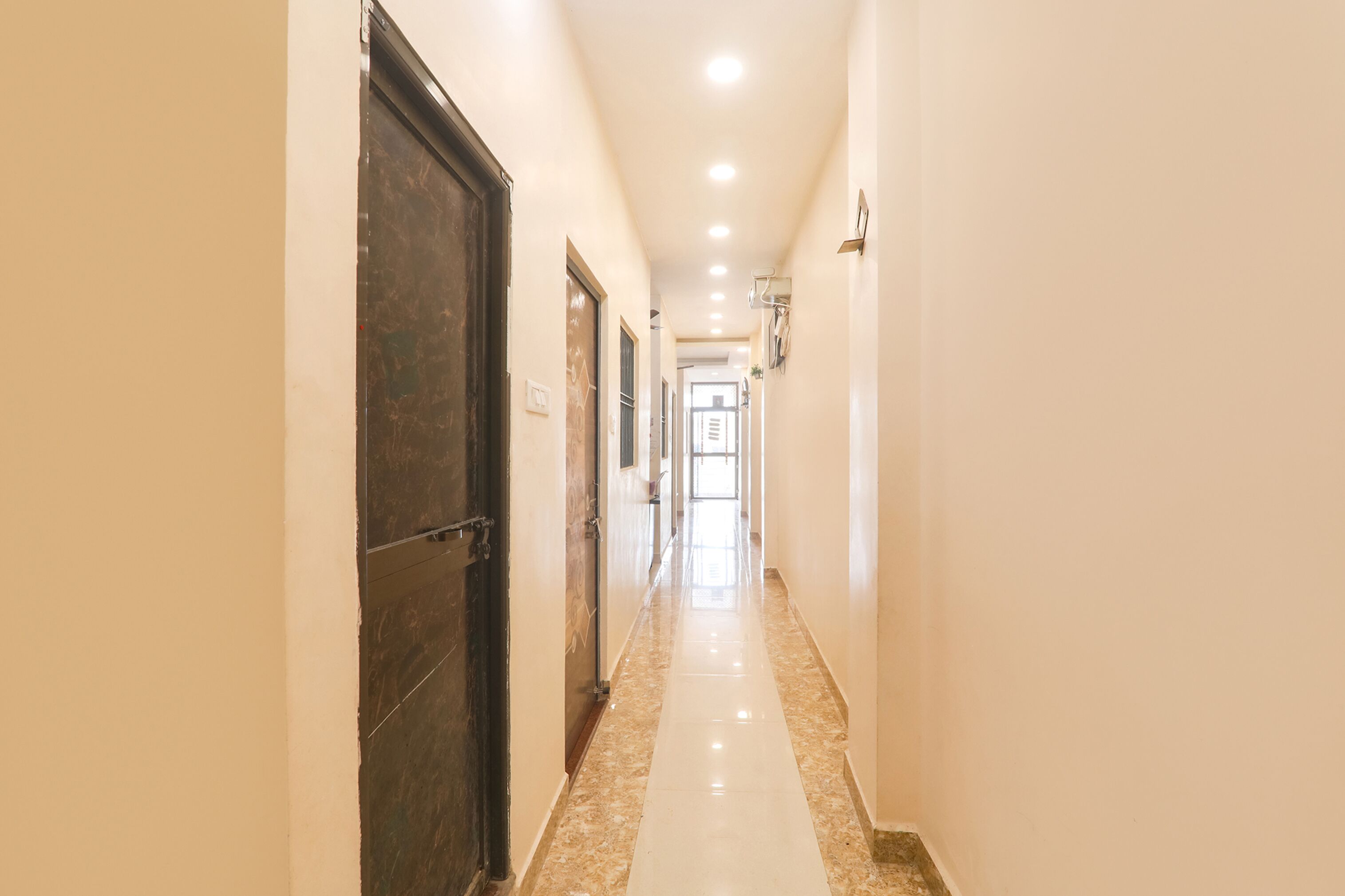 A long, well-lit hallway with a marble floor and a dark door on the left.