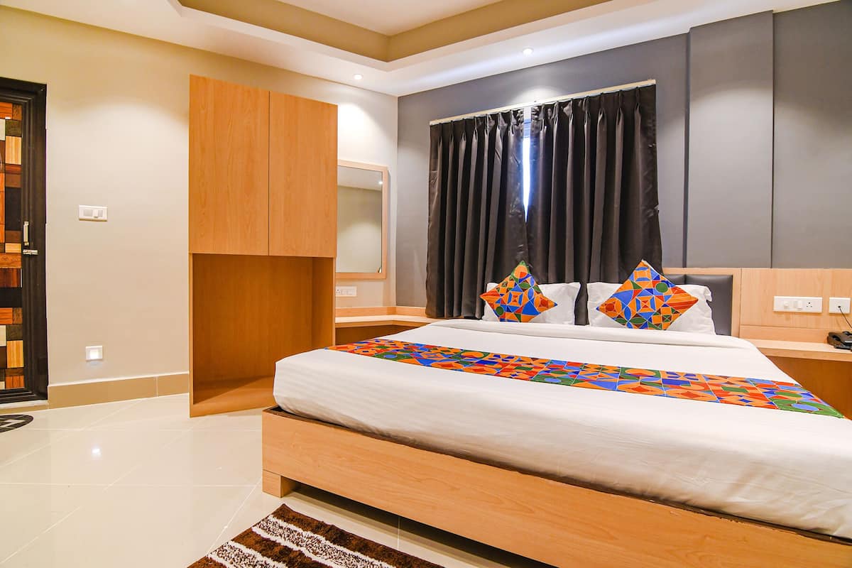 Una habitación de hotel moderna con una cama grande, un armario de madera, un espejo y una ventana con cortinas.