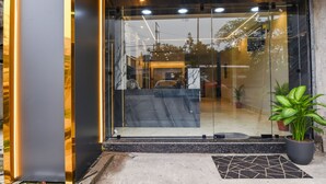 Entrada de um edifício moderno com portas de vidro, um vaso de planta e um tapete de azulejos.