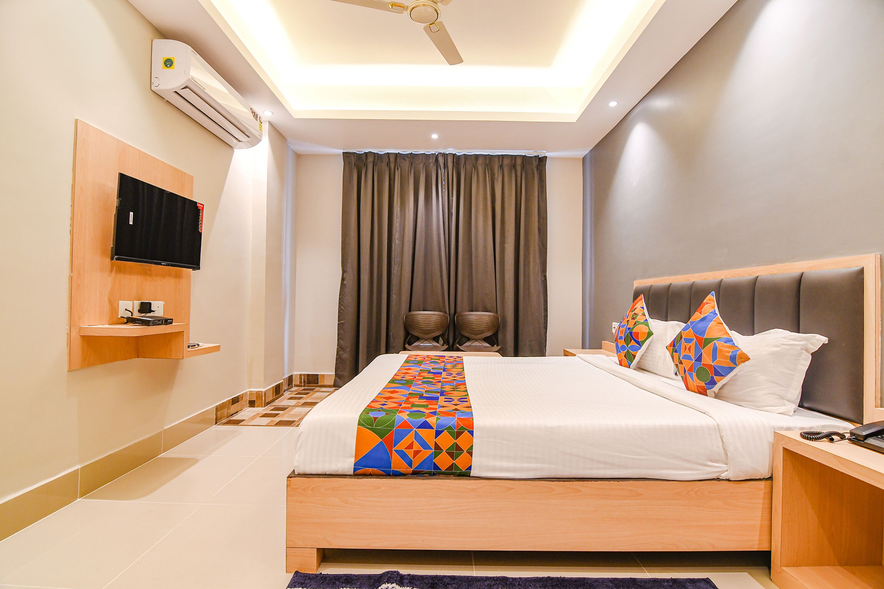 Une chambre d’hôtel moderne équipée d’un lit, d’un téléviseur fixé au mur, d’un ventilateur de plafond et d’un appareil de climatisation.
