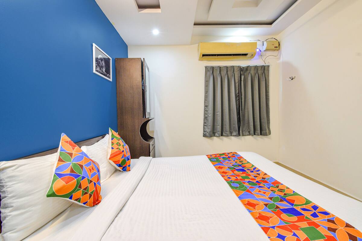 A hotel room with a bed, pillows, a curtain, and a wall-mounted air conditioner.