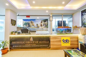 Un mostrador de recepción con un letrero del Grupo de Hoteles Broholic, con sucursales en Hi-Tech City, Gachibowli, Kondapur y Kukatpally.