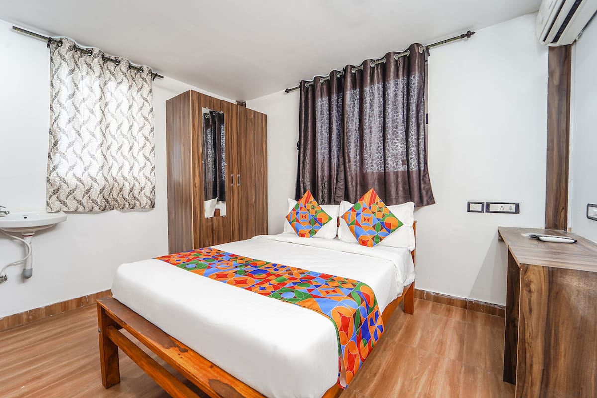 A bedroom with a wooden bed, a bedside table, a nightstand, a wardrobe, a bathroom sink, and a shower curtain.