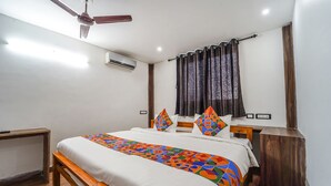 A bedroom with a bed, a wooden bench, a ceiling fan, an air conditioning unit, and a window with curtains. - Fabhotel Chakra (Coimbatore)